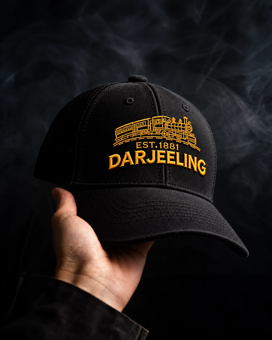 Black Darjeeling cap held in hand, showing golden train embroidery